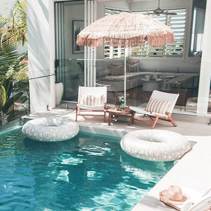 Pool area with lounge chairs, inflatable rings, and a thatched umbrella on a patio.