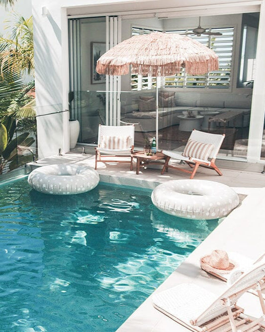Pool area with lounge chairs, inflatable rings, and a thatched umbrella on a patio.