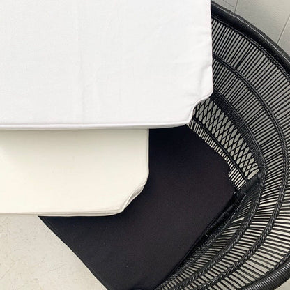 Black wicker chair with a white cushion on a light wooden floor.