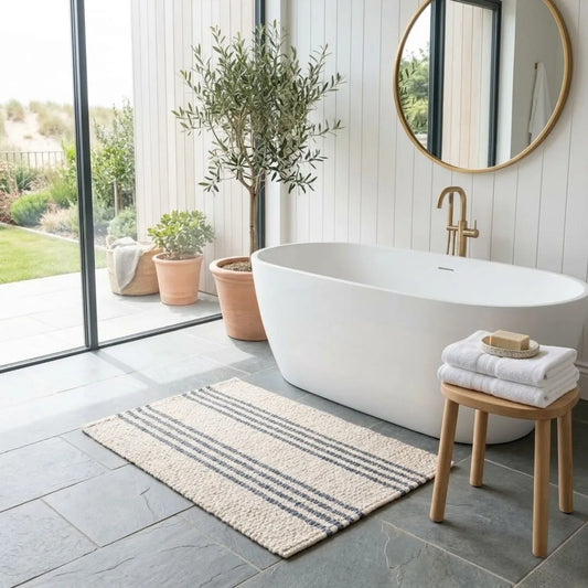 Modern bathroom with a freestanding bathtub, wooden stool, and potted plants.