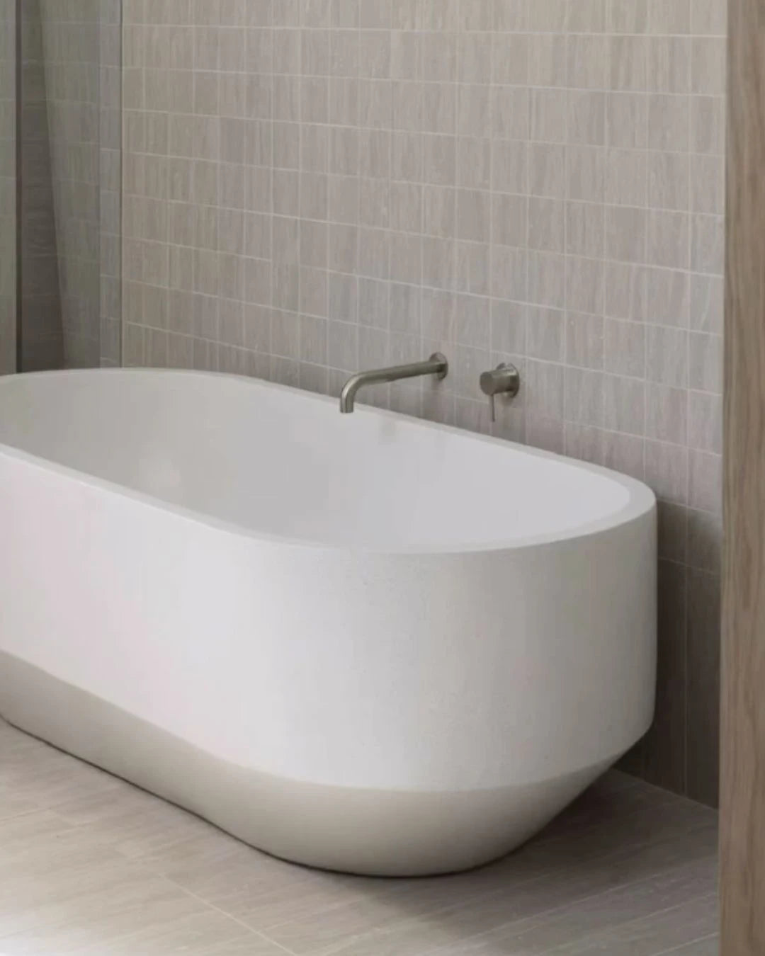 Modern white freestanding bathtub in a bathroom with tiled walls.