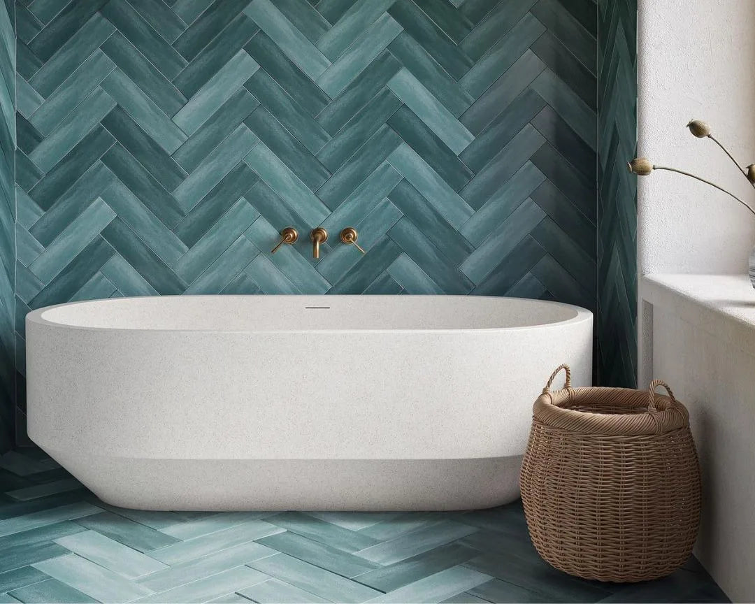 Modern bathroom with a white freestanding bathtub against a teal herringbone tiled wall.