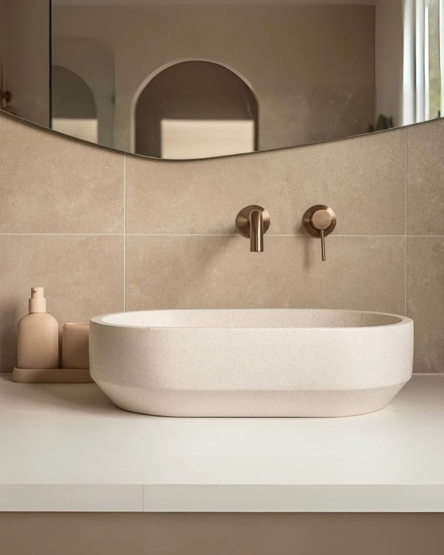 Beige bathroom with a round sink and gold fixtures.