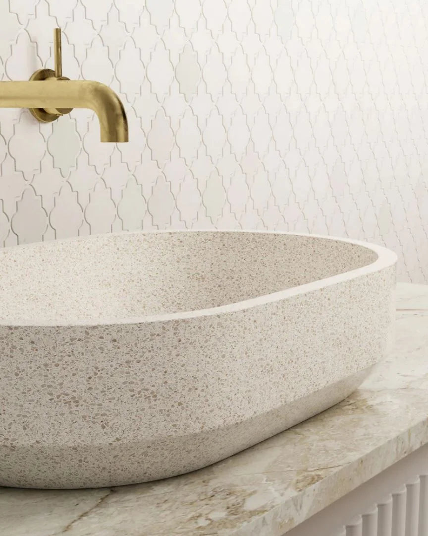 Stone sink with gold faucet against a patterned wall