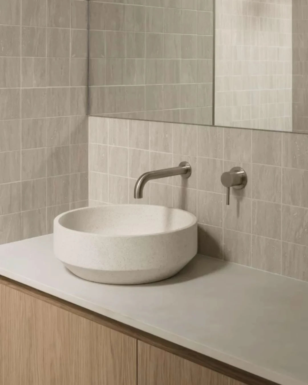 Bathroom vanity with a white sink and silver faucet against a tiled wall.