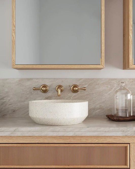 Bathroom vanity with marble sink, gold faucet, and wooden cabinet.