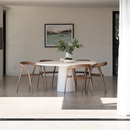 Modern dining area with a Sun Republic Elio round white microcement table and wooden chairs, featuring a framed picture on the wall.