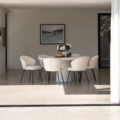 Modern dining room with white chairs and a round table, featuring a framed picture on the wall.