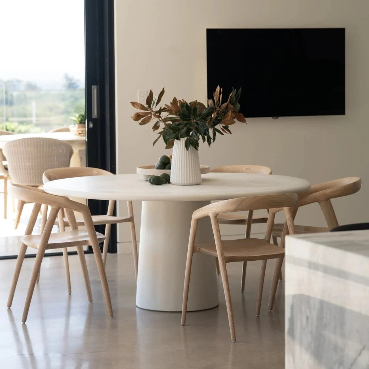 Modern dining area with a white round table and chairs, featuring a television on the wall.