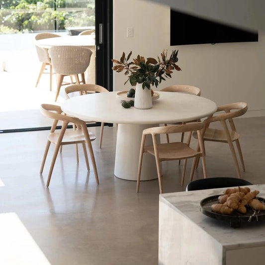 Modern dining area with a white round table and wooden chairs in a bright room.