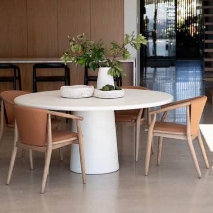 Modern dining area with a white round table and wooden chairs. Featuring the Elio Round Microcement Dining Table – Seashell Finish from Sun Republic