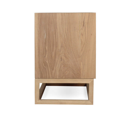 A modern wooden cabinet or side table with a natural oak finish, featuring a tall rectangular upper section and a geometric open base, shown against a plain white background.