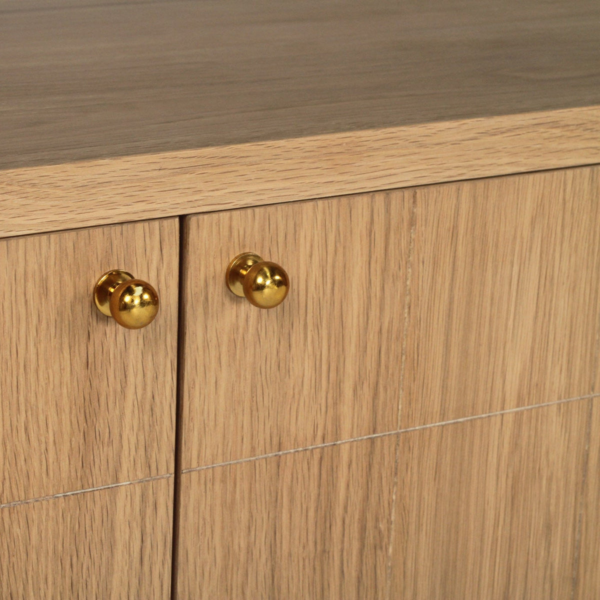 Close-up of a wooden cabinet with two doors, featuring round polished brass knobs and a medium brown wood grain finish.