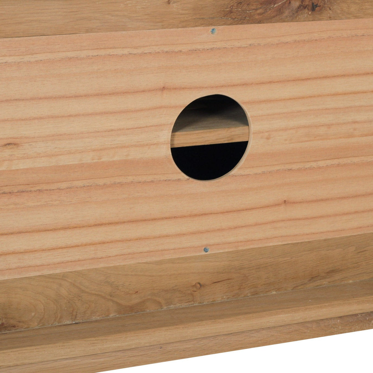 Close-up of a light natural wood surface with a circular cutout showing a dark interior, likely part of a wooden furniture piece or cabinet.