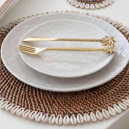White ceramic plates with gold cutlery on a woven placemat.