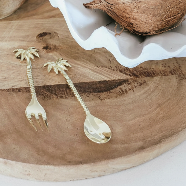 Palm tree-shaped fork and spoon on a wooden board with a coconut and candle in the background.