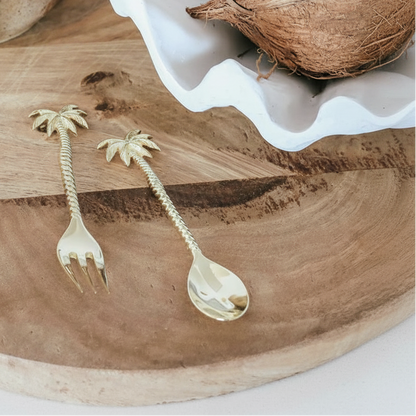 Palm tree-shaped fork and spoon on a wooden board with a coconut and candle in the background.