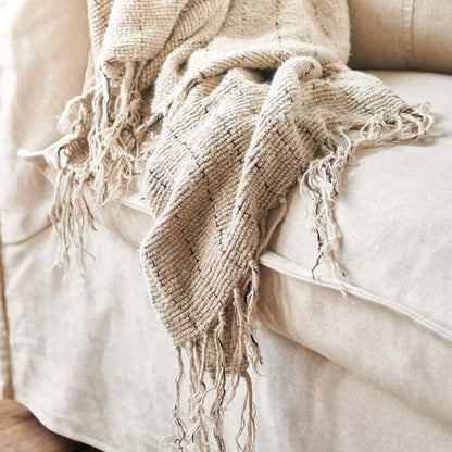 mayla textured throw blanket with fringes draped over a beige sofa