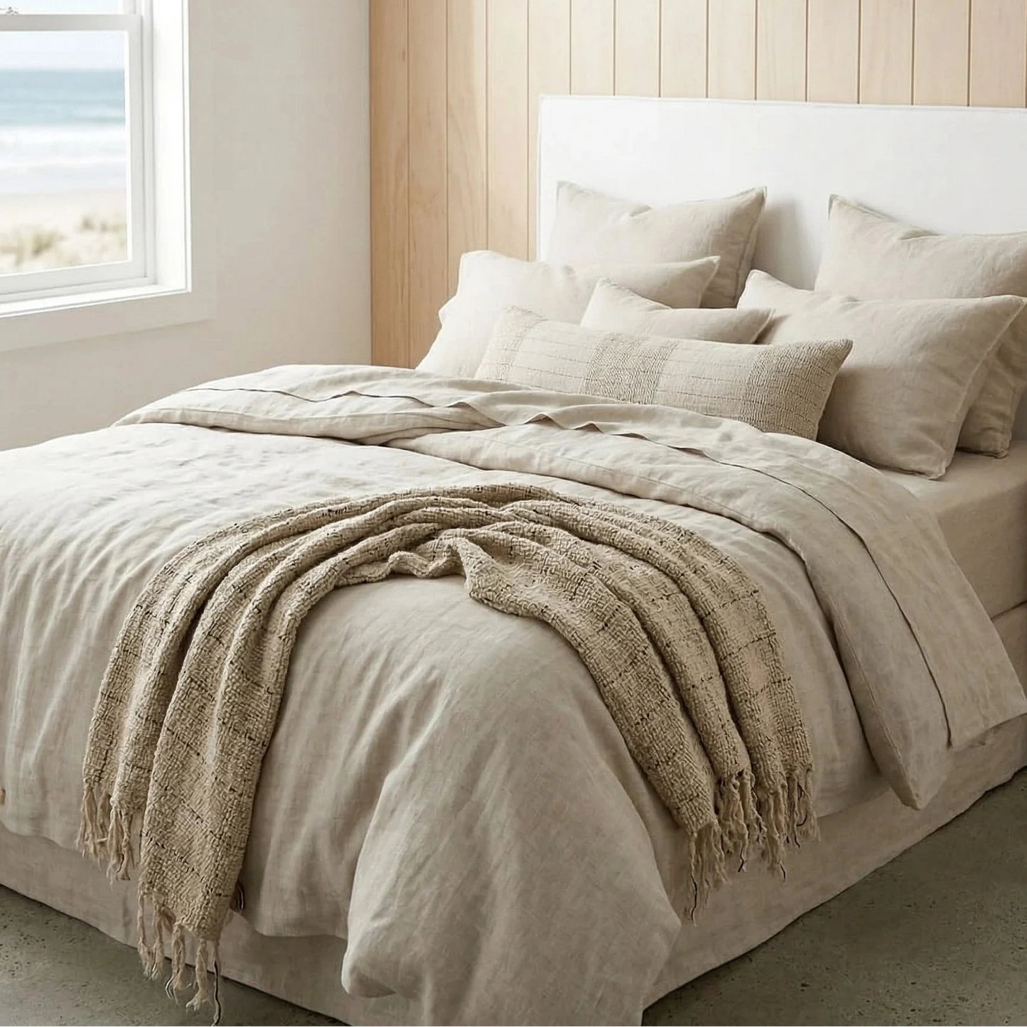 Neatly made bed with beige bedding in a bedroom with wooden walls and a window.