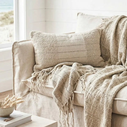 Beige sofa with textured throw blanket and pillow in a bright room.