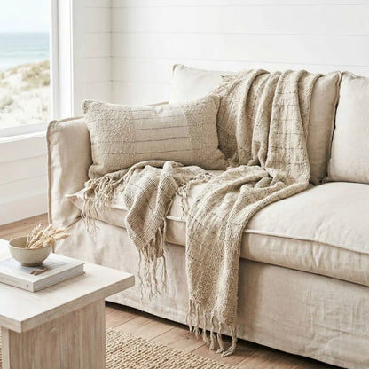 Beige sofa with textured throw blanket in a room with large windows.