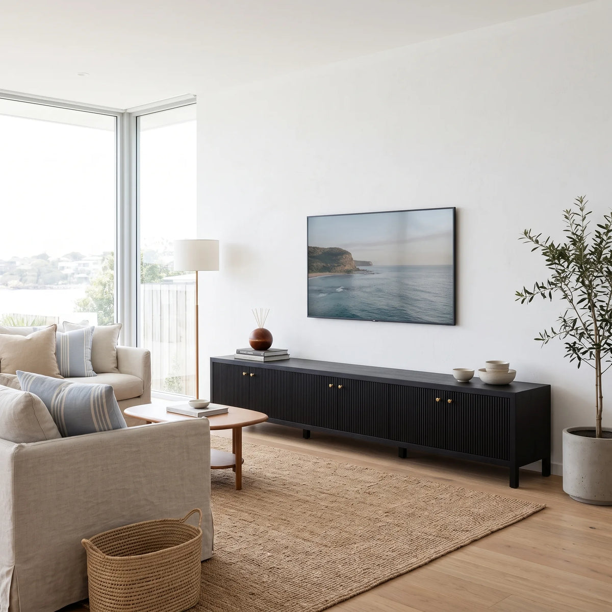 A modern living room scene featuring a long black media console with brass knobs, styled with a landscape TV on top, in front of a white wall.