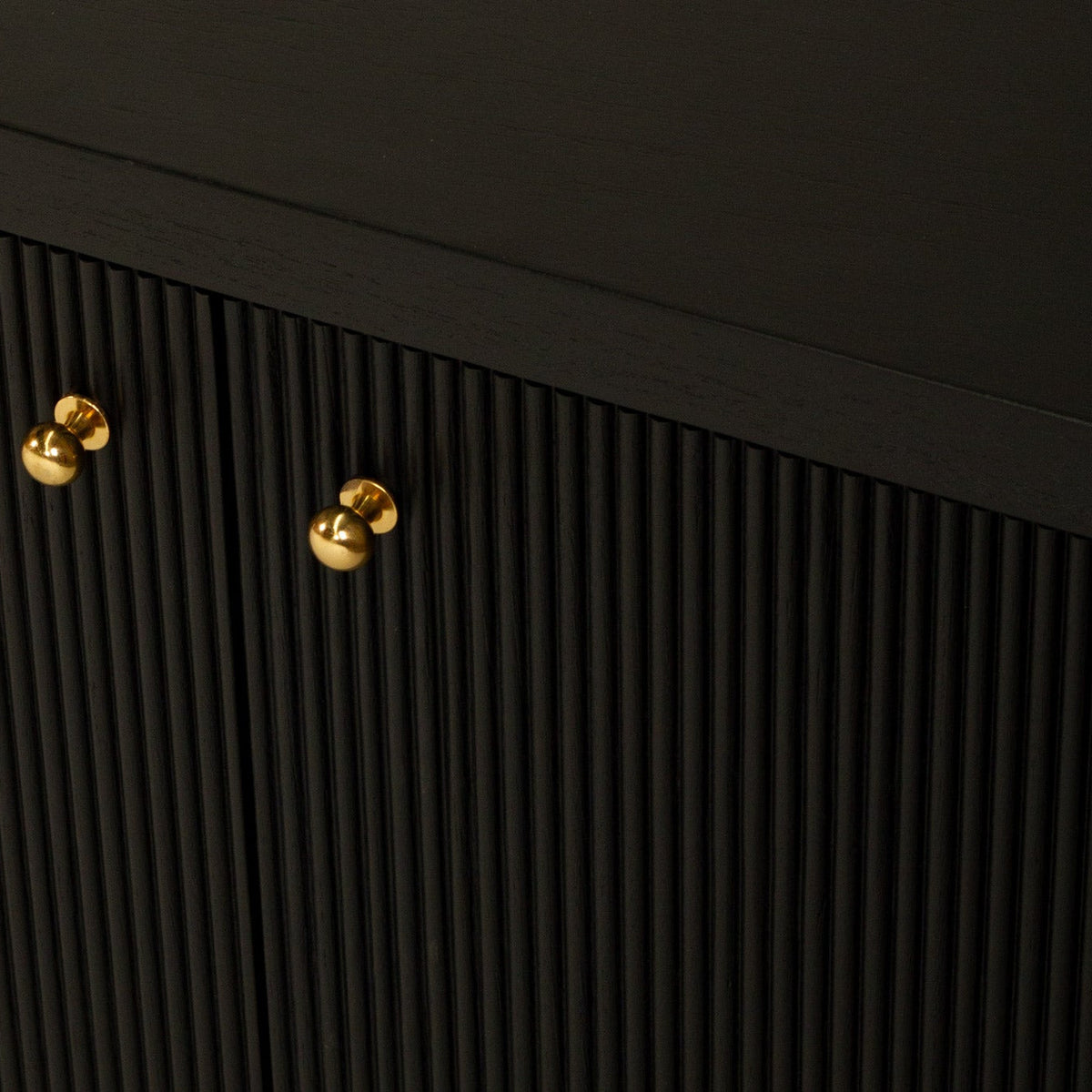 Close-up of a black ribbed cabinet door with two round gold knobs, shown against a matching dark background.