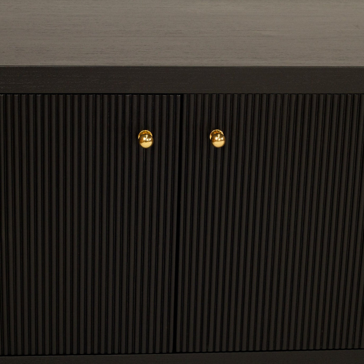Close-up of a dark wood cabinet with vertically ribbed doors and two small round gold knobs, set against a dark gray textured wall.