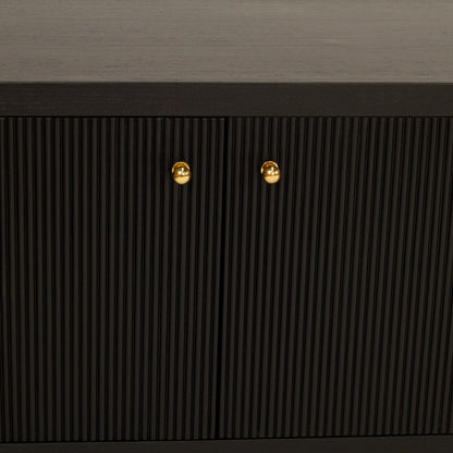 Close-up of a dark wood cabinet with vertically ribbed doors and two small round gold knobs, set against a dark gray textured wall.