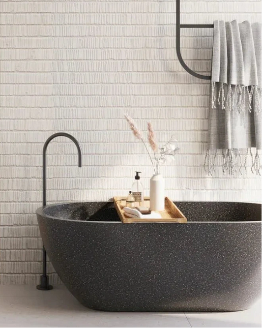 Modern bathroom with a black freestanding bathtub, white tiled wall, and gray towel.