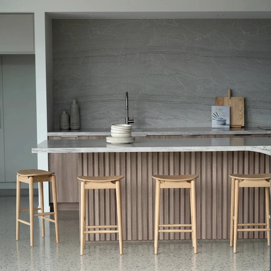 Four wooden bar stools in a modern kitchen setting with a countertop and cabinets.