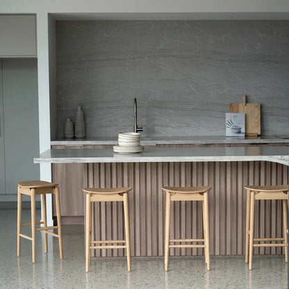 Four wooden bar stools in a modern kitchen setting with a countertop and cabinets.