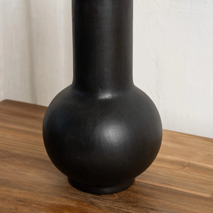 Close up of a black vase on a wooden surface with a white background
