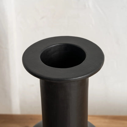 Close up of a black vase on a wooden surface with a white 