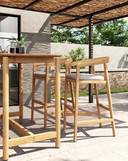 Outdoor patio setting with wooden bar stools and table under a thatched roof.