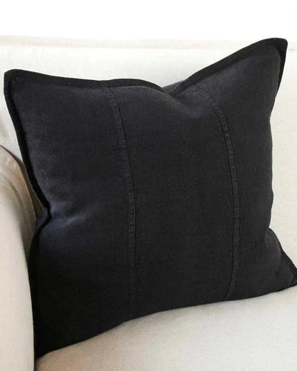 A black linen cushion with a plush feather insert, displayed on a white sofa.