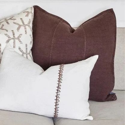 A chocolate brown linen cushion with a plush feather insert, displayed on a sofa with other cushions.