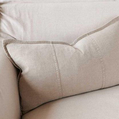 Close-up of a natural beige linen cushion with a plush feather insert, showcasing the fabric texture and stitching details.