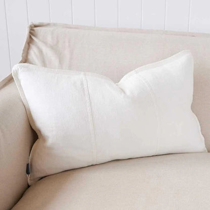 Beige sofa with a white pillow against a white paneled wall.