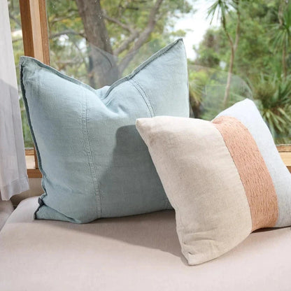 Two cushions on a sofa with a window view of trees.