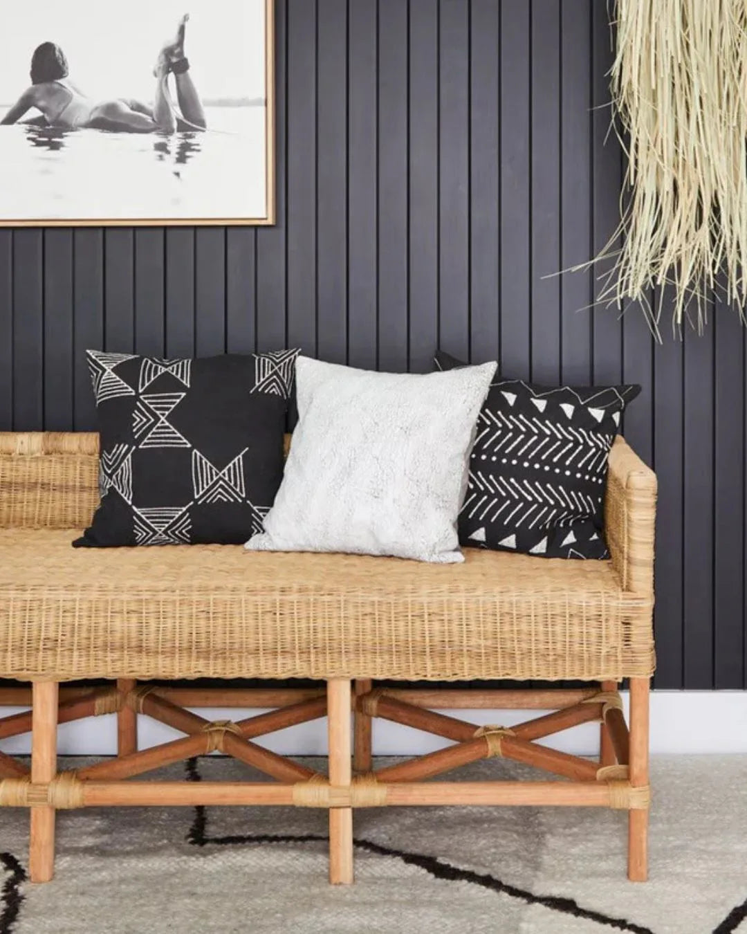 Wicker bench with patterned cushions against a dark paneled wall.