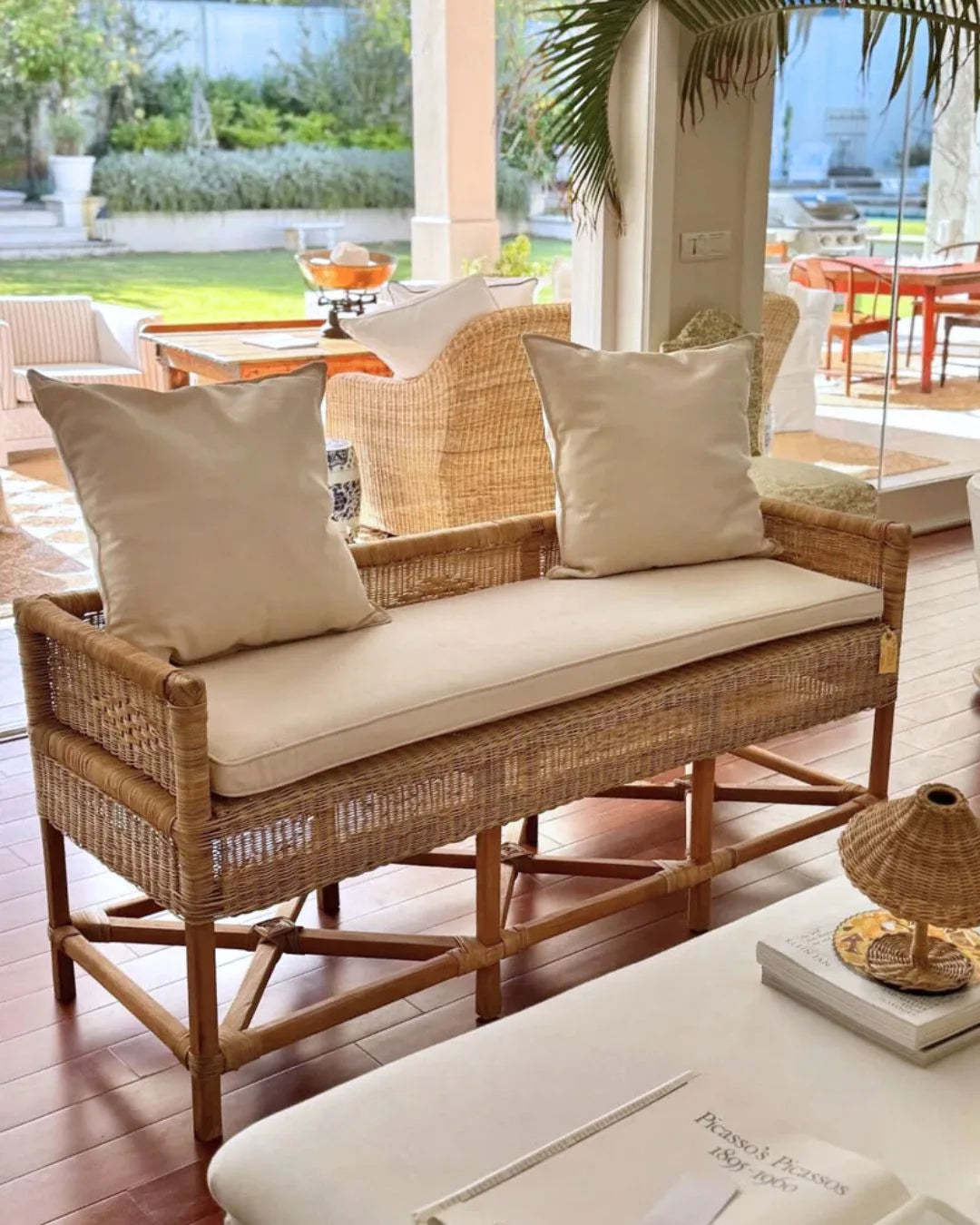 Wicker bench with beige cushions on a patio