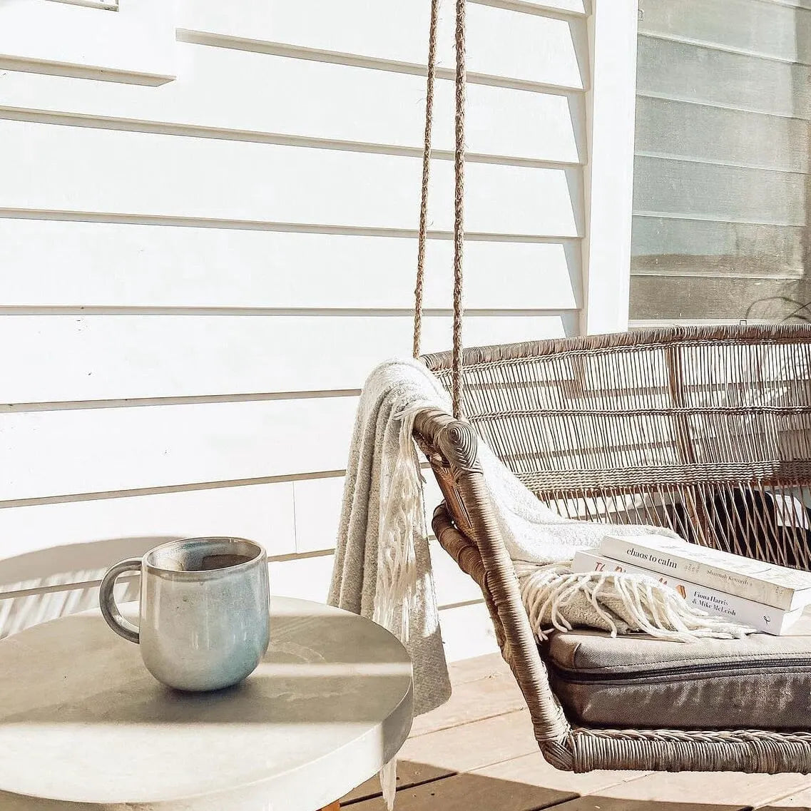 Hanging chair with books and a mug on a small table in a bright room.