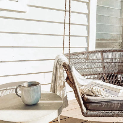 Hanging chair with books and a mug on a small table in a bright room.