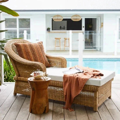 Wicker outdoor lounge chair with cushions on a wooden deck by a pool