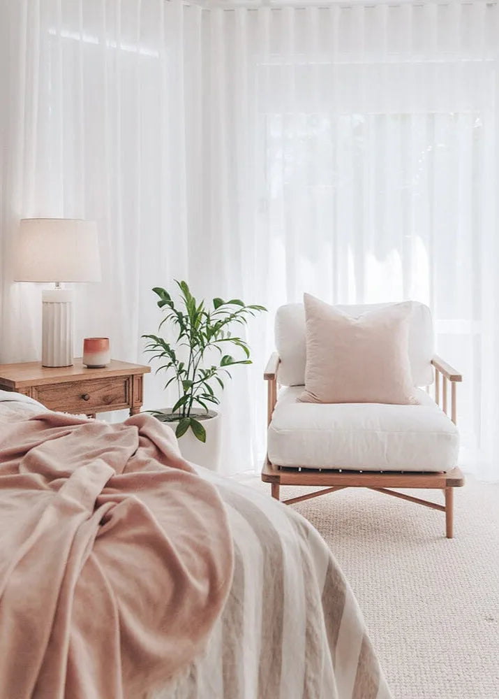 Cozy bedroom with a bed, chair, and lamp under sheer curtains.
