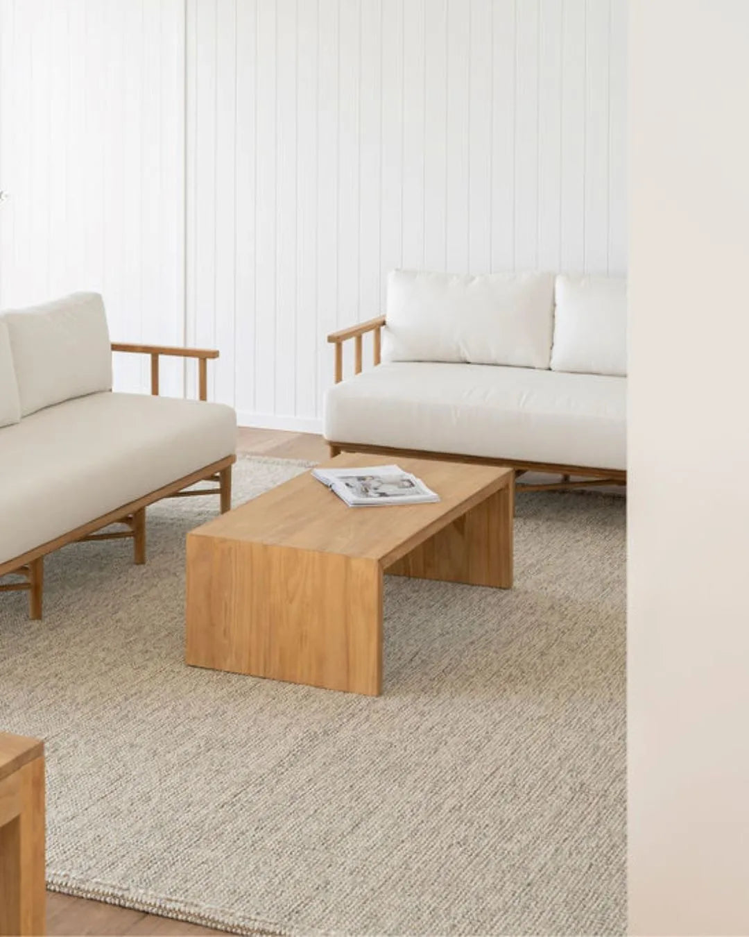 Teak outdoor sofa with white cushions in a outdoor living space with teak coffee table and side table.