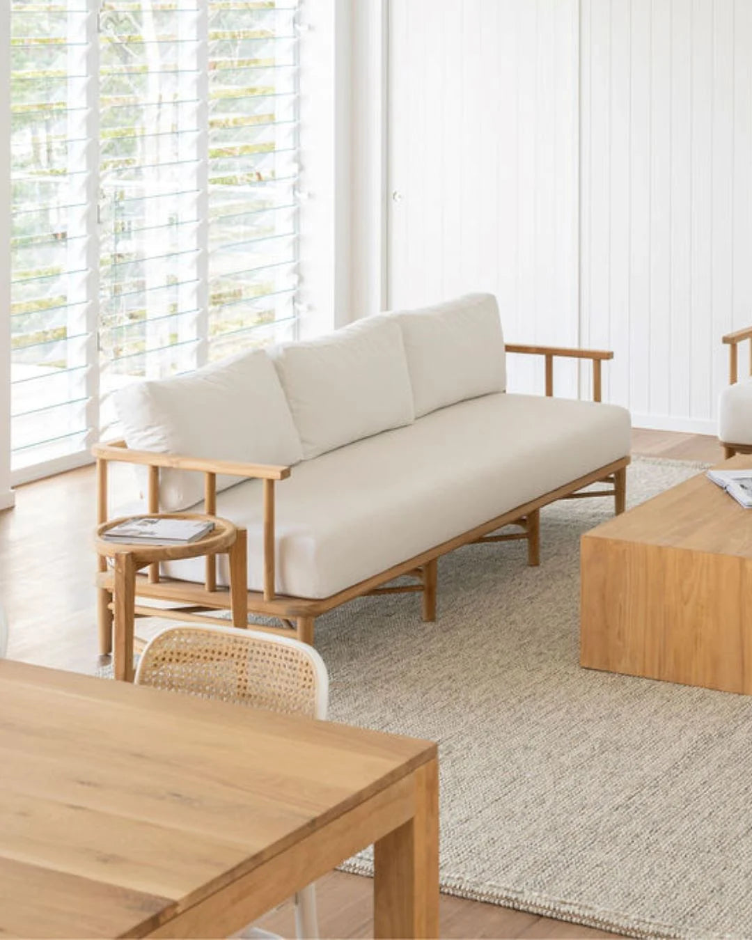 Teak outdoor sofa with white cushions in a outdoor living space with teak coffee table and side table.