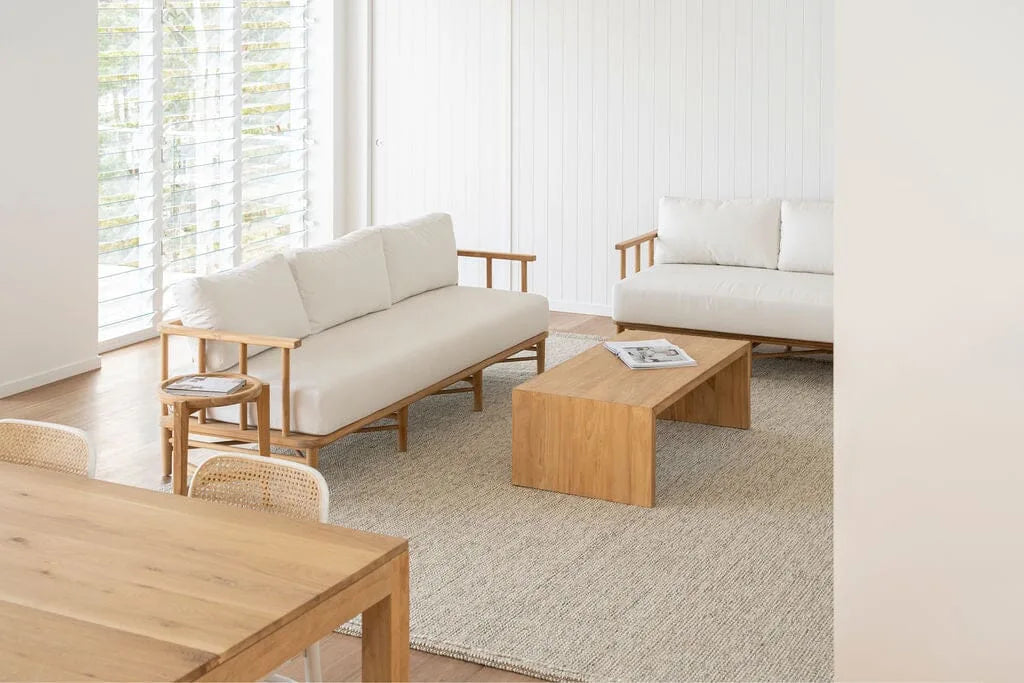 Teak outdoor sofa with white cushions in a living space with teak coffee table and side table.