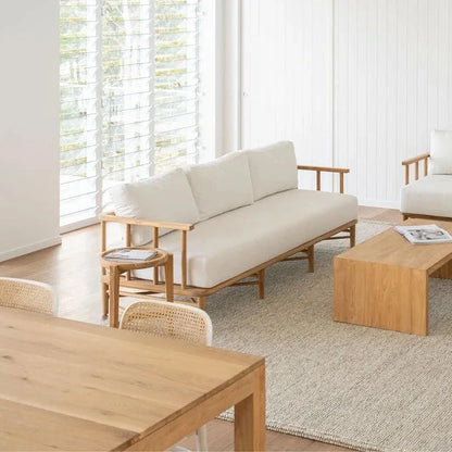 Teak outdoor sofa with white cushions in a living space with teak coffee table and side table.